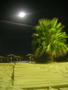 Foto sacada desde el paseo maritimo al acceso a la playa con la luna llena al fondo reflejando su luz en el mar.